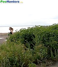 Cute young blondie makes water behind a lush shrub